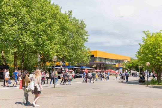 Studierende auf dem Campus Nord mit der Hauptmensa im Hintergrund im Sommer