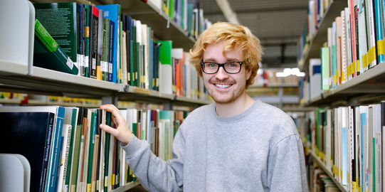 Studierender steht an einem Bücherregal in der Bibliothek.
