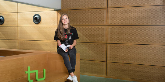 Eine Studentin mit Buch und TU-Logo.
