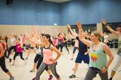 Teilnehmerinnen und Teilnehmer eines Fitness-Kurses in einer großen Sporthalle