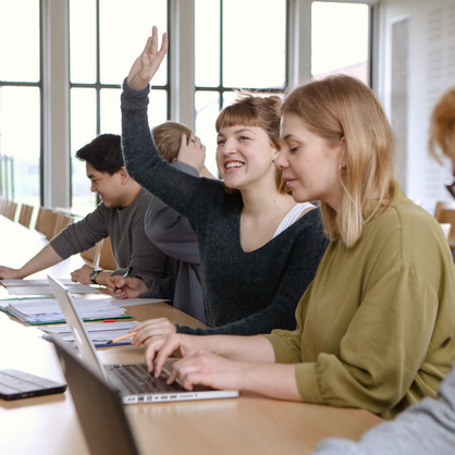 Studierende im Seminar Fünf Studierende sitzen in einem Seminarraum an Tischen. Eine Studentin hebt ihre Hand.