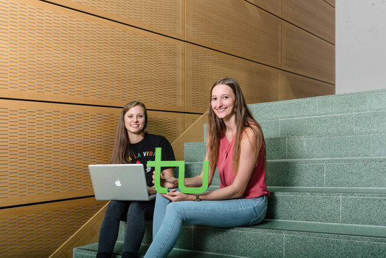 Zwei Studentinnen sitzen mit Laptop und TU-Logo auf einer Treppe.